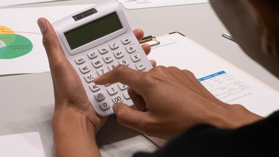 Hands using a calculator beside financial paperwork.