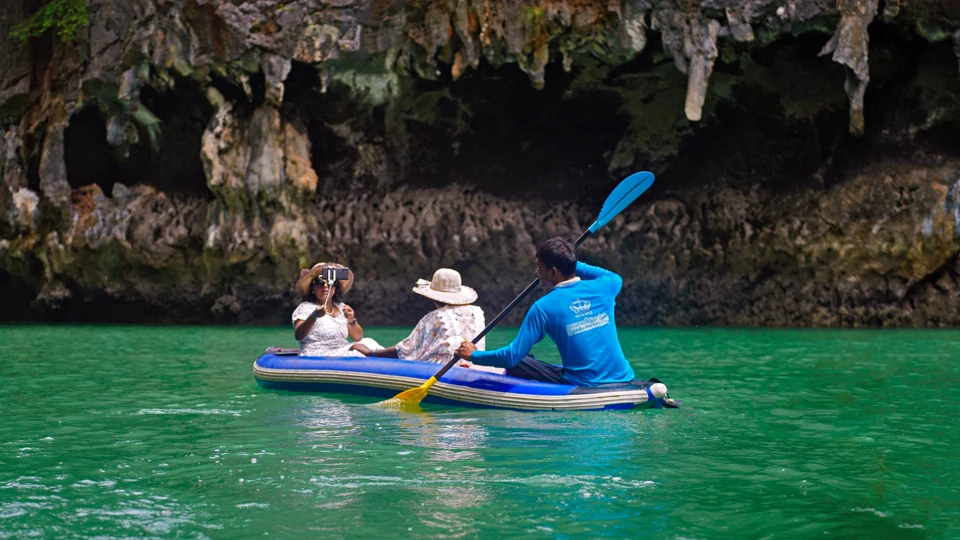 Travelers sharing a kayak beside limestone cliffs in Krabi, Thailand.