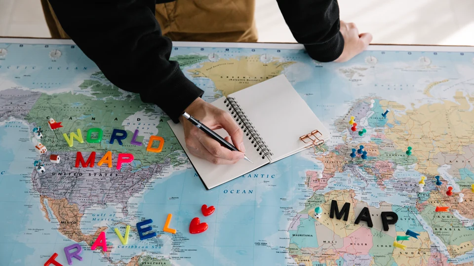 A person writing travel notes in a notebook laid on a world map.