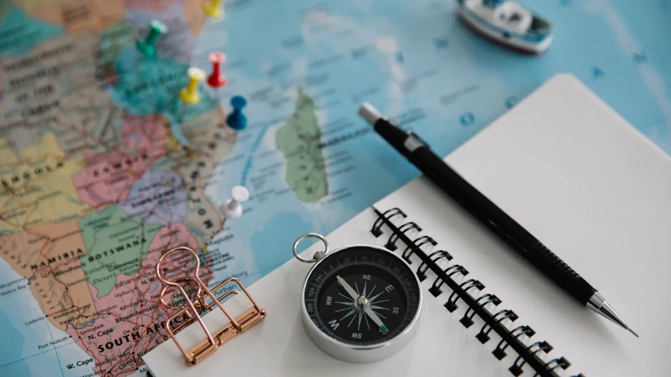 A notebook, compass and route markers arranged on a travel map.
